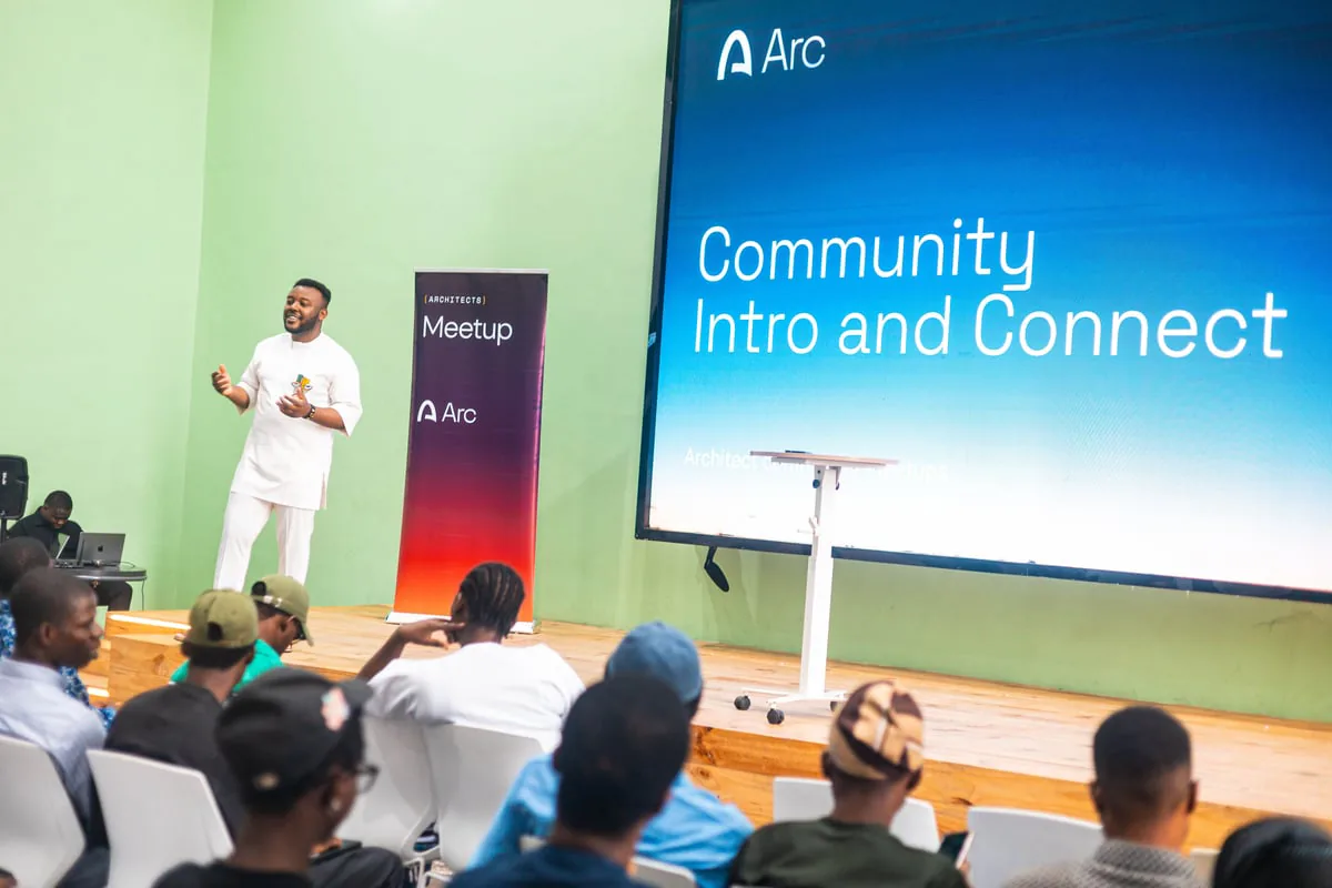 Cyon speaking on stage at the Arc community meetup in Benin City, beside a screen reading Community Intro and Connect.