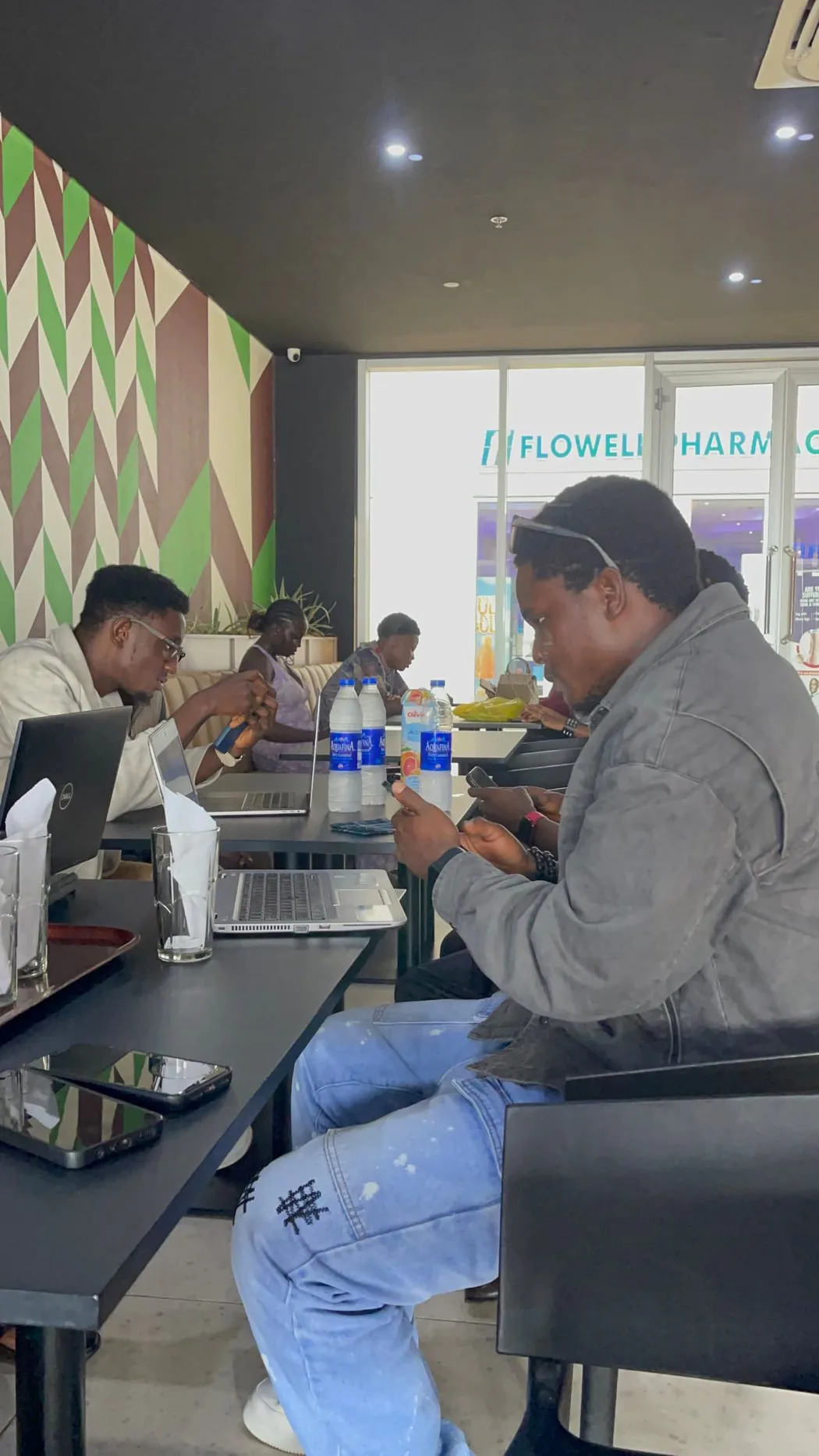 Two builders heads-down on laptops and phones during a cafe working session in Benin City.