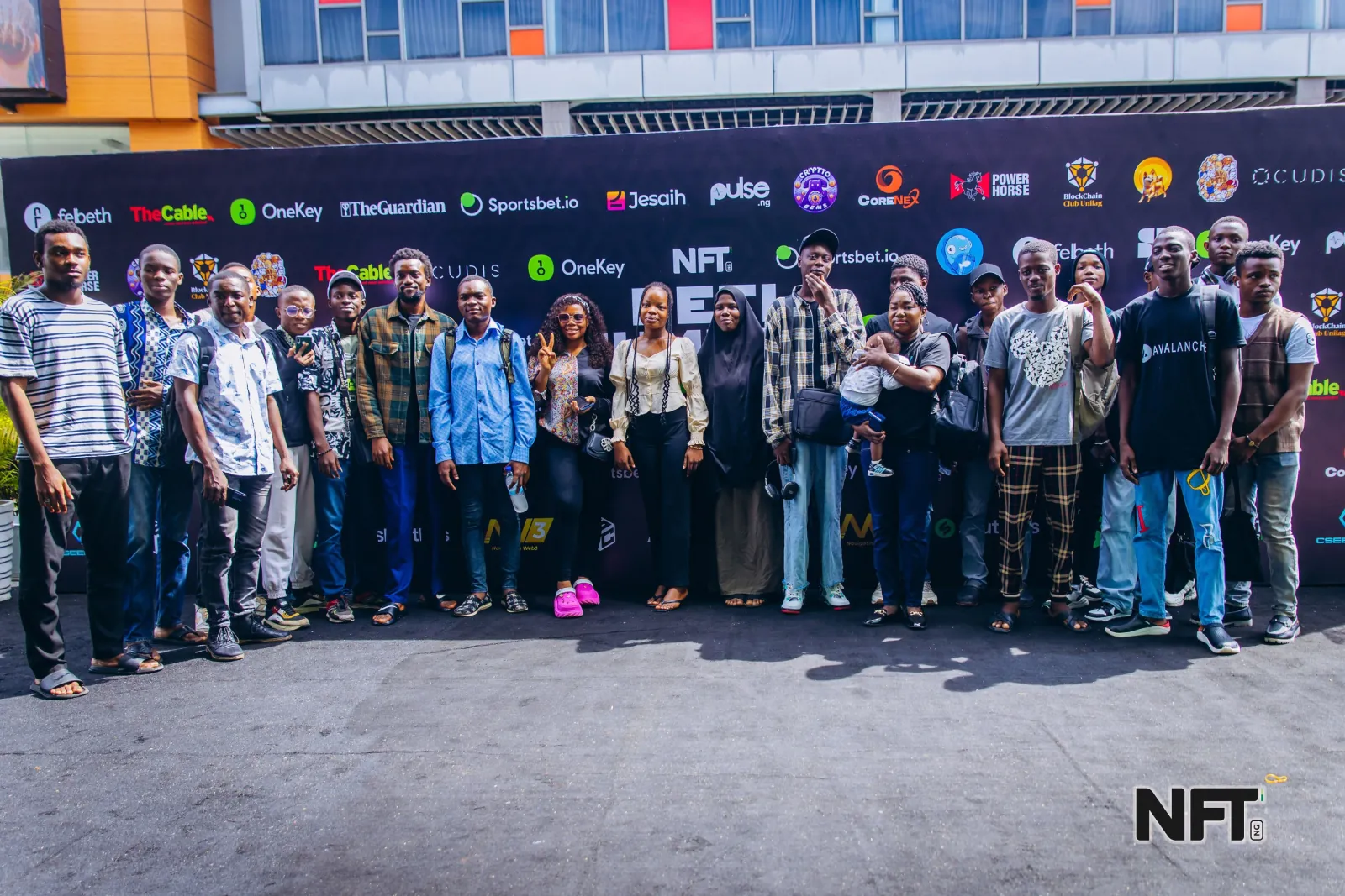 A large group of attendees posing together in front of a black sponsor wall covered in Web3 partner logos at an in-person community event.