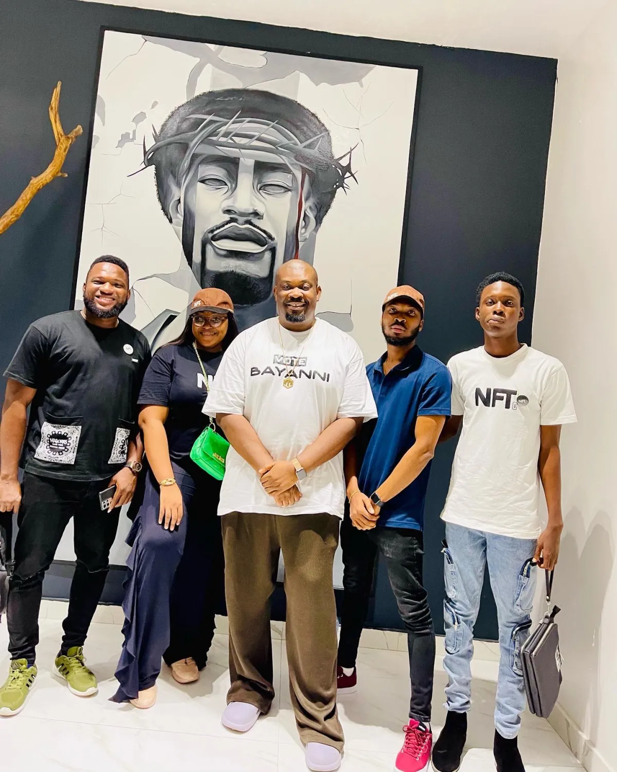 Five organisers standing arm in arm in front of a large portrait mural painted on the venue wall.